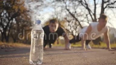 两个高加索青年运动员在日落时在秋天的公园里奋力前行。 运动男孩在户外训练。 重点放在